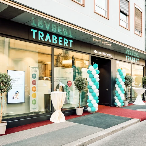 Modernes Hörakustik-Fachgeschäft Trabert mit Ballondekoration und rotem Teppich.