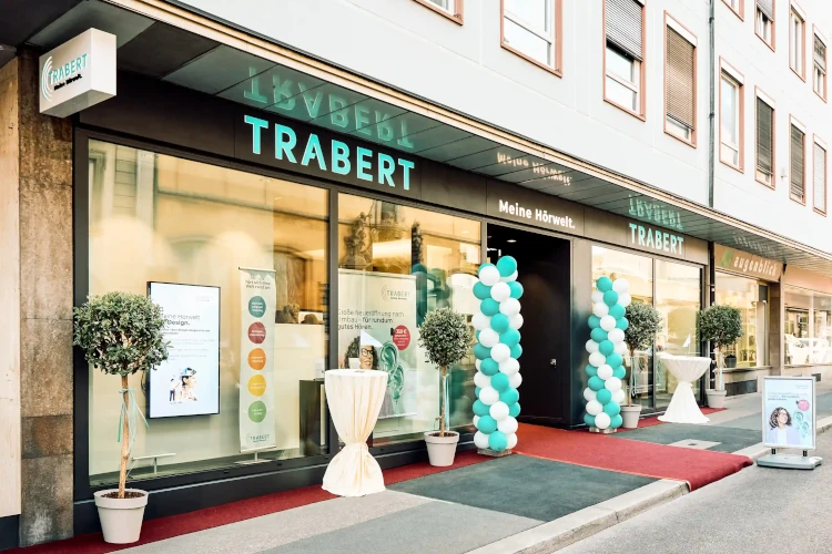 Moderne Hörakustik-Filiale Trabert mit Schaufenstern, Ballondekoration und Infotafeln.